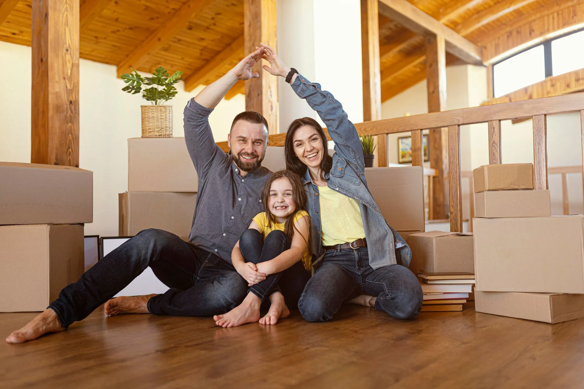 Family making a house shape with their arms, surrounded by moving boxes.